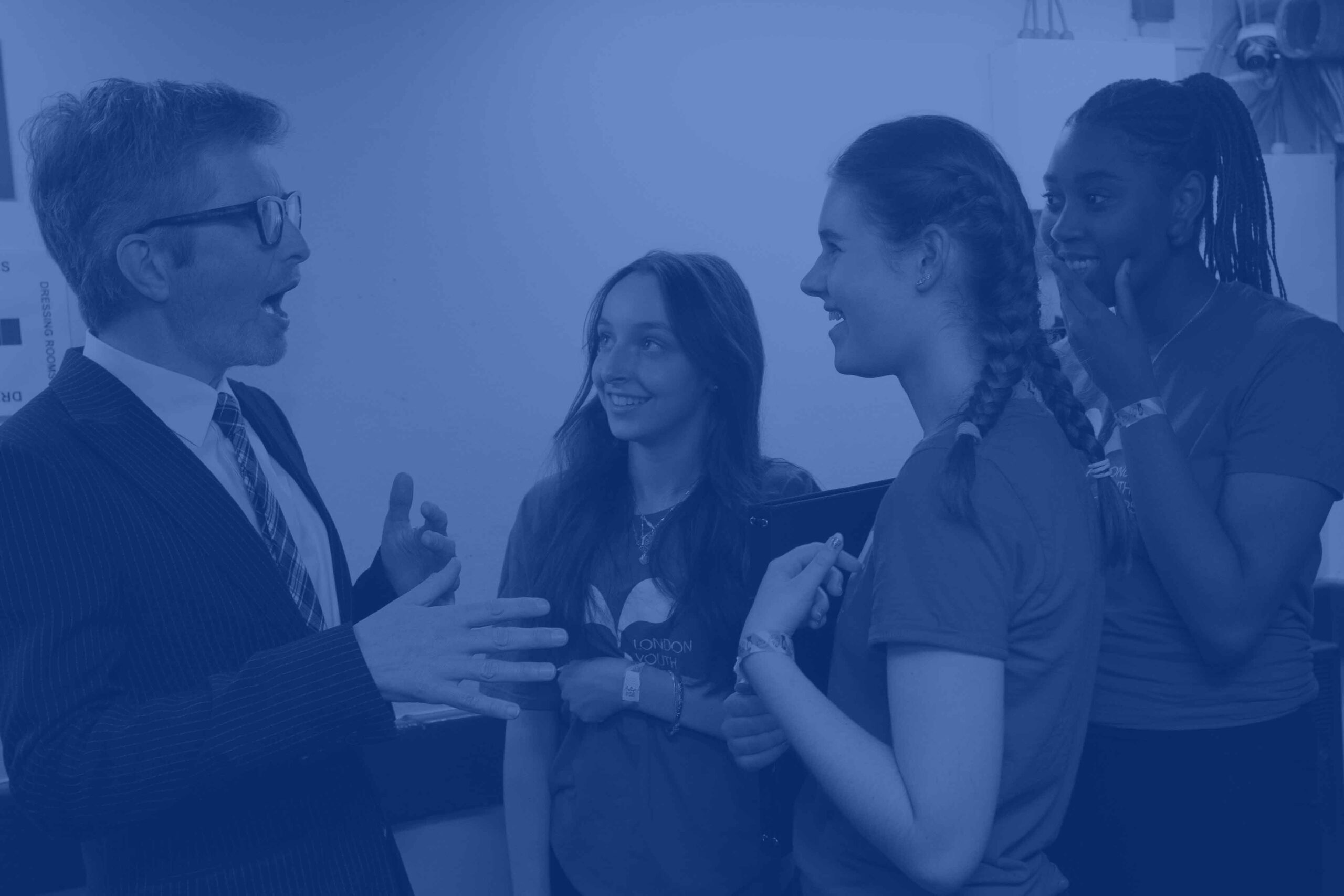 A blue image of three LYC members talking to LYC Honorary Patron Gareth Malone