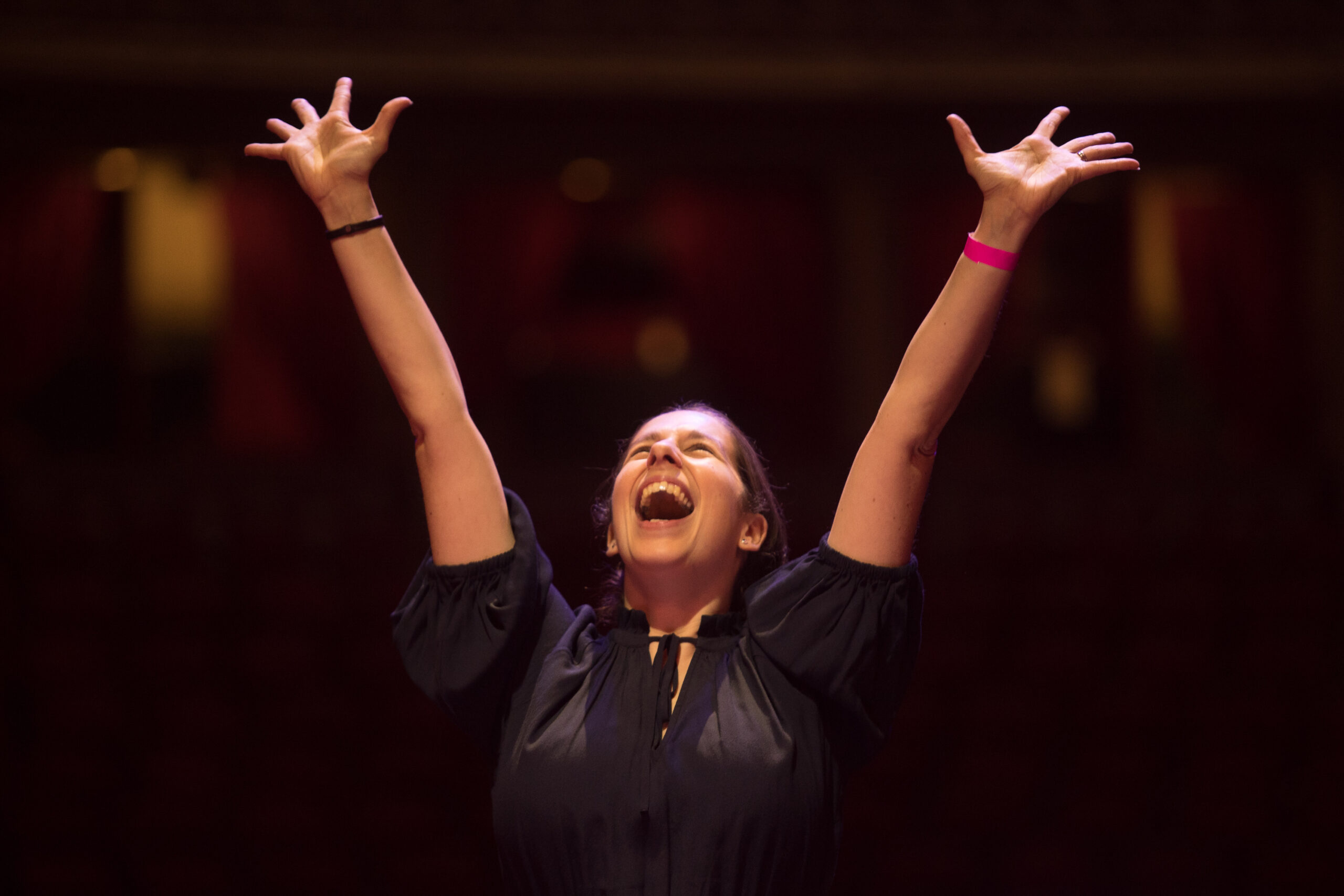 Rachel Staunton with her arms up, looking up with a joyful expression on her face, wearing black concert uniform