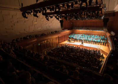 A choir on stage wearing teal T shirts, as seen from the balcony.